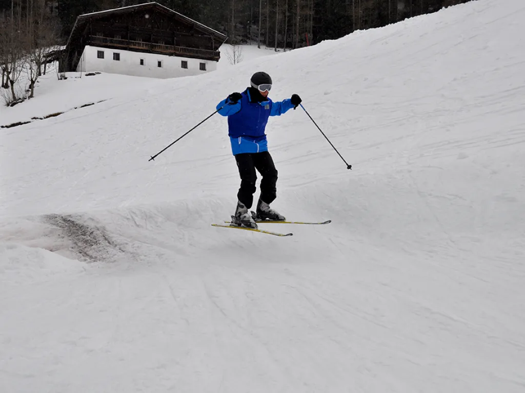 Skifahrer in blauer Jacke auf der Piste vor einem Stadel.